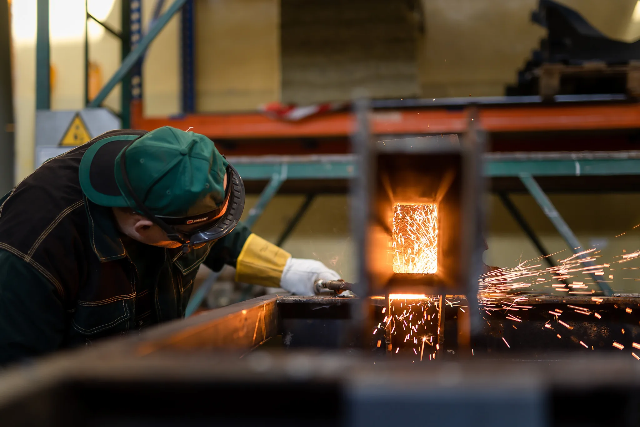 A welder cutting steel section at the bench, sparks running off the cut